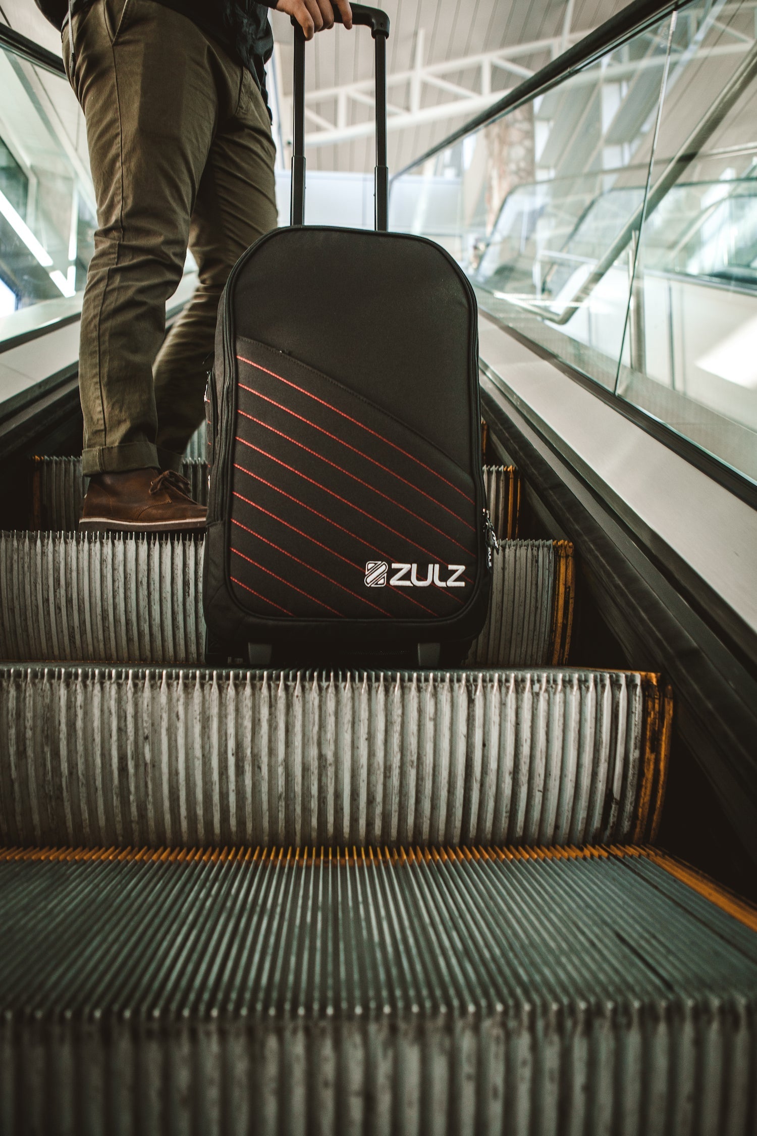 A traveler riding an escalator with their carry-on in view