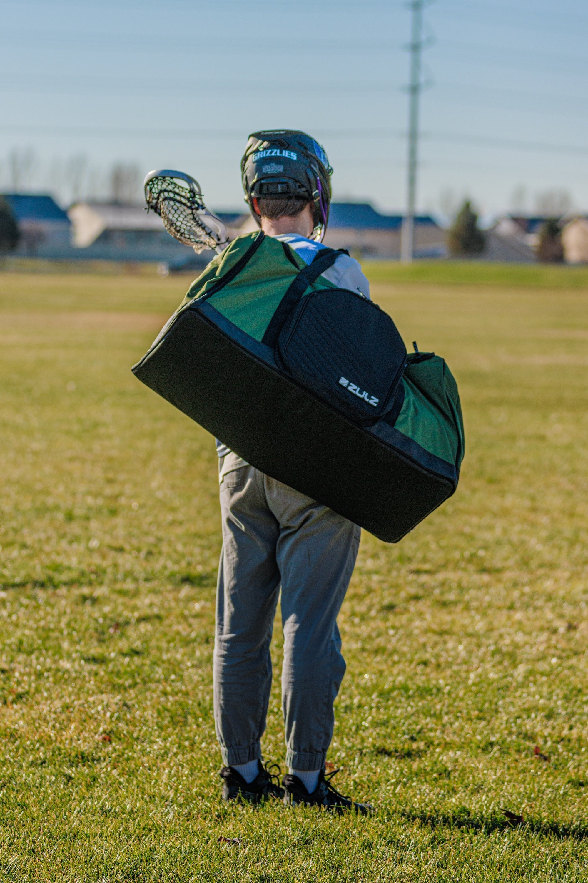 A lacrosse player standing in a field carrying duffle over shoulder