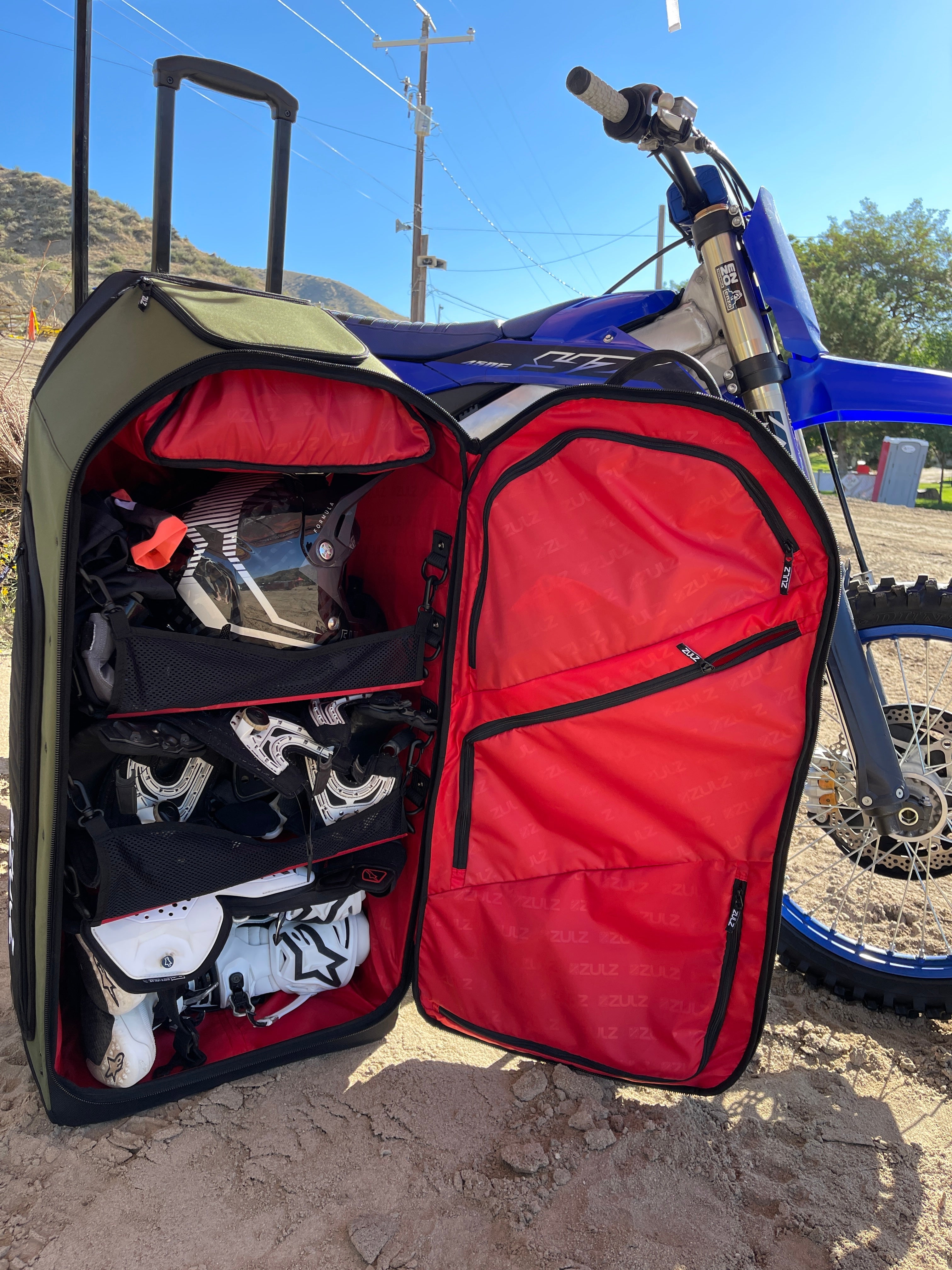 Dirtbike in background with gearbag open showing bags capability to carry a lot while being organized due to shelving system